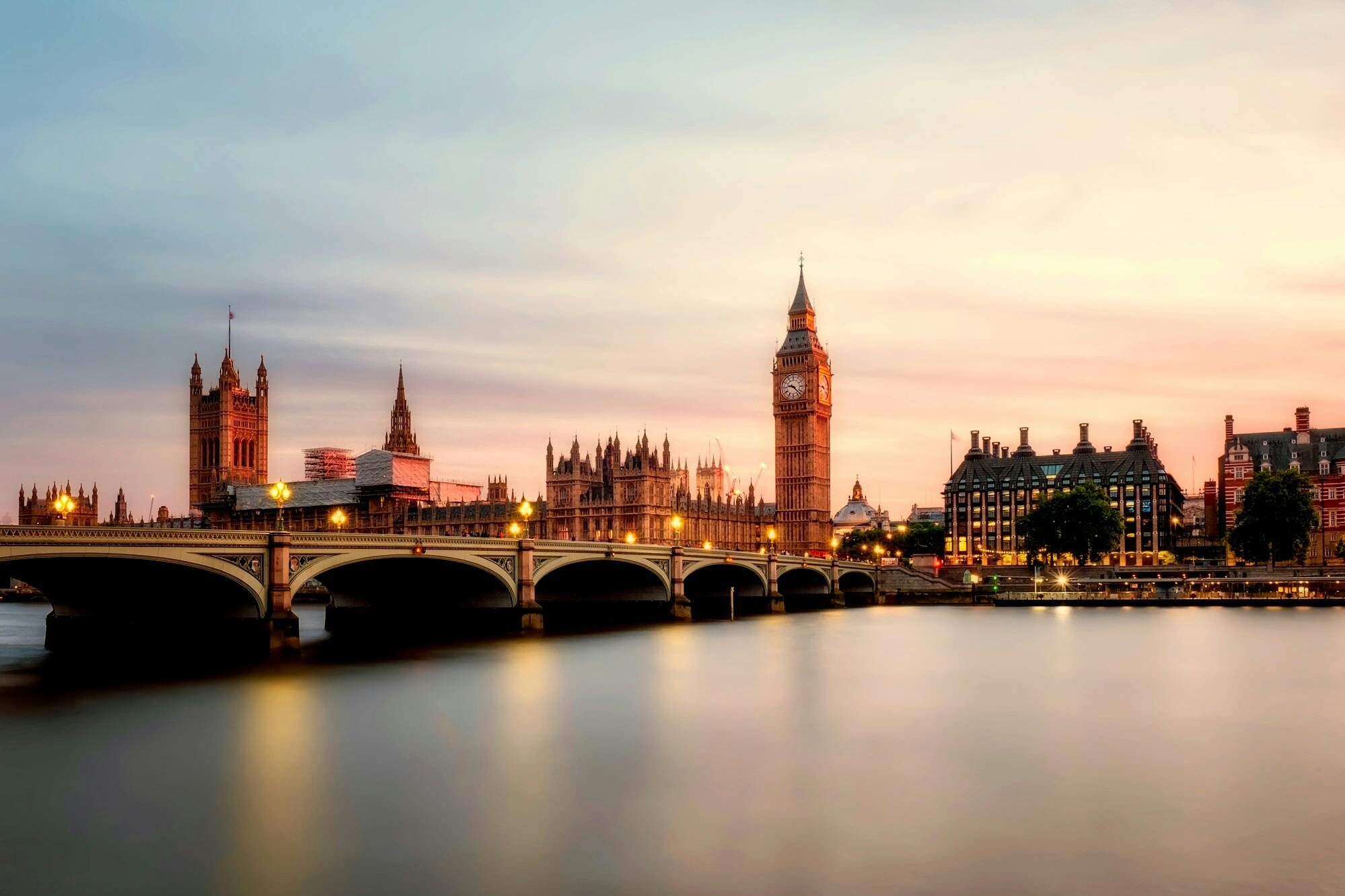 Sunset view of Big Ben and the Houses of Parliament in London, England, with Westminster Bridge crossing the River Thames.